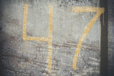 Kalıplı gri beton duvarda 47 numara sarı çizikler ve çatlaklar var..