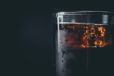 Siyah arka planda, buzlu ve damlacıklı bir bardakta soda.