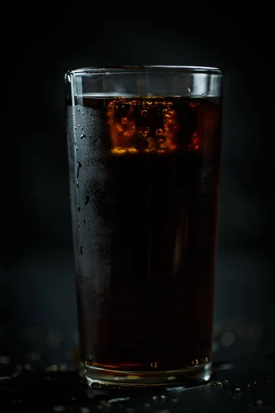 Soda in a glass on a black background with ice cubes and drops