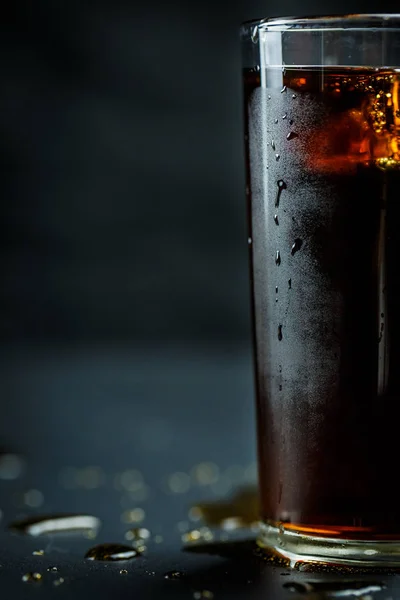 Soda in a glass on a black background with ice cubes and drops