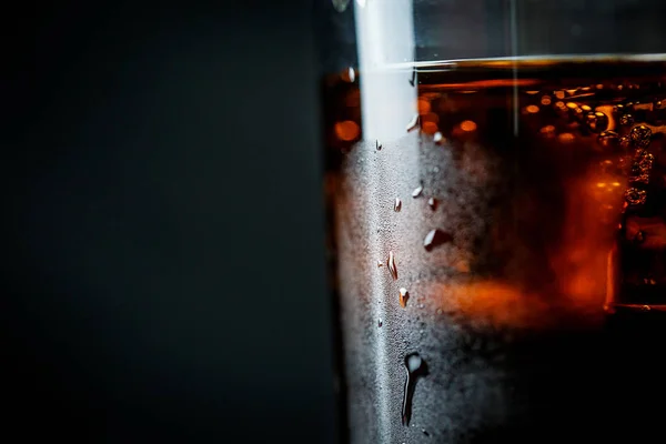 Soda in a glass on a black background with ice cubes and drops