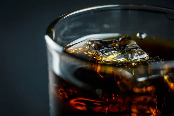 Soda in a glass on a black background with ice cubes and drops