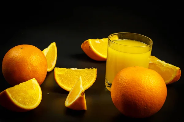 杯子里的新鲜橙汁和黑色背景上的橙子片 — 图库照片