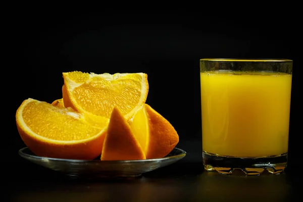 杯子里的新鲜橙汁和黑色背景上的橙子片 — 图库照片
