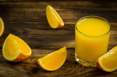 Bir bardak portakal suyu ve portakal dilimleri ahşap bir masada.