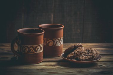 Kahverengi kil kahve fincanları ve ahşap bir masada sıcak renklerde lezzetli çikolatalı kurabiyeler.