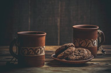Kahverengi kil kahve fincanları ve ahşap bir masada sıcak renklerde lezzetli çikolatalı kurabiyeler.
