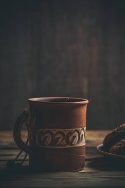 Kahverengi kil kahve fincanları ve ahşap bir masada sıcak renklerde lezzetli çikolatalı kurabiyeler.