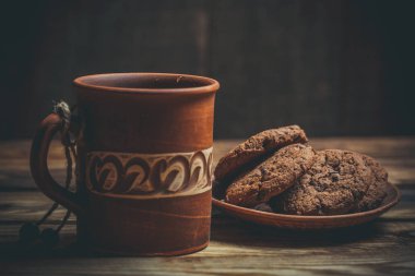 Kahverengi kil kahve fincanları ve ahşap bir masada sıcak renklerde lezzetli çikolatalı kurabiyeler.