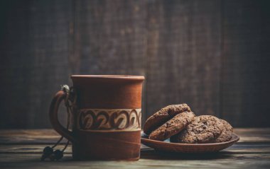 Kahverengi kil kahve fincanları ve ahşap bir masada sıcak renklerde lezzetli çikolatalı kurabiyeler.