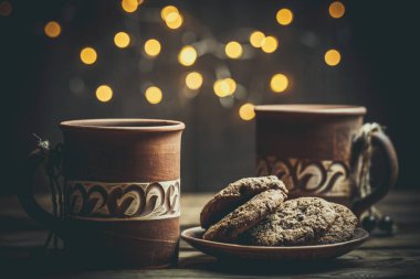 Kahverengi kil kahve fincanları ve ahşap bir masada sıcak renklerde lezzetli çikolatalı kurabiyeler.