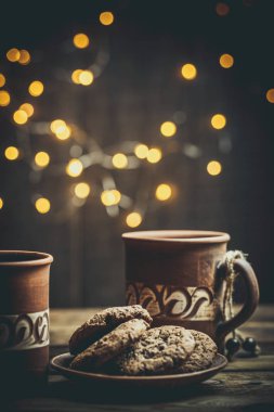 Kahverengi kil kahve fincanları ve ahşap bir masada sıcak renklerde lezzetli çikolatalı kurabiyeler.