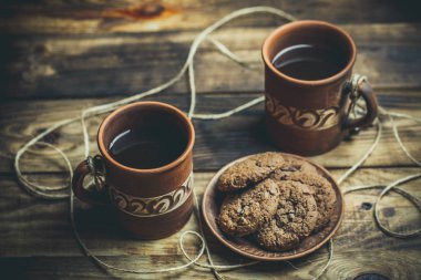 Kahverengi kil kahve fincanları ve ahşap bir masada sıcak renklerde lezzetli çikolatalı kurabiyeler.