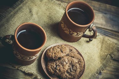 Kahverengi kil kahve fincanları ve ahşap bir masada sıcak renklerde lezzetli çikolatalı kurabiyeler.