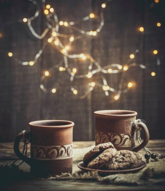 Kahverengi kil kahve fincanları ve ahşap bir masada sıcak renklerde lezzetli çikolatalı kurabiyeler.