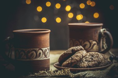 Kahverengi kil kahve fincanları ve ahşap bir masada sıcak renklerde lezzetli çikolatalı kurabiyeler.