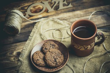 Kahverengi kil kahve fincanları ve ahşap bir masada sıcak renklerde lezzetli çikolatalı kurabiyeler.