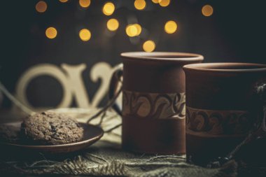 Kahverengi kil kahve fincanları ve ahşap bir masada sıcak renklerde lezzetli çikolatalı kurabiyeler.