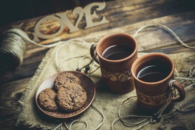 Kahverengi kil kahve fincanları ve ahşap bir masada sıcak renklerde lezzetli çikolatalı kurabiyeler.