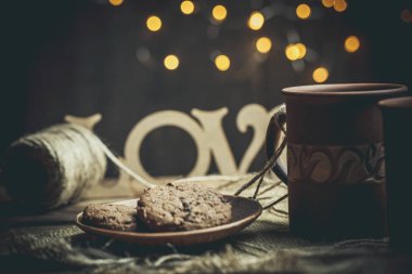 Kahverengi kil kahve fincanları ve ahşap bir masada sıcak renklerde lezzetli çikolatalı kurabiyeler.