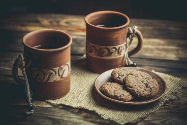 Kahverengi kil kahve fincanları ve ahşap bir masada sıcak renklerde lezzetli çikolatalı kurabiyeler.