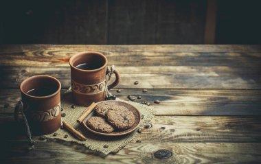 Kahverengi kil kahve fincanları ve ahşap bir masada sıcak renklerde lezzetli çikolatalı kurabiyeler.