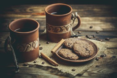 Kahverengi kil kahve fincanları ve ahşap bir masada sıcak renklerde lezzetli çikolatalı kurabiyeler.
