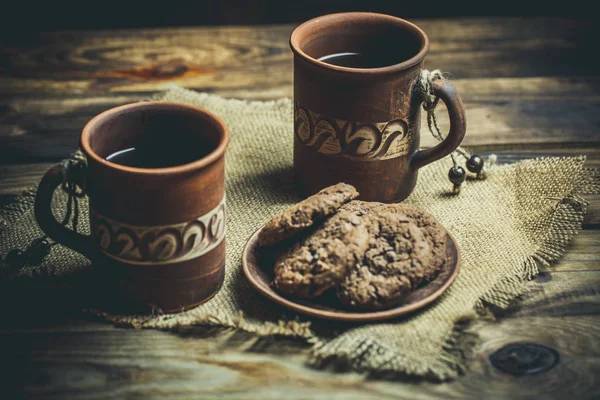 Kahverengi kil kahve fincanları ve ahşap bir masada sıcak renklerde lezzetli çikolatalı kurabiyeler.