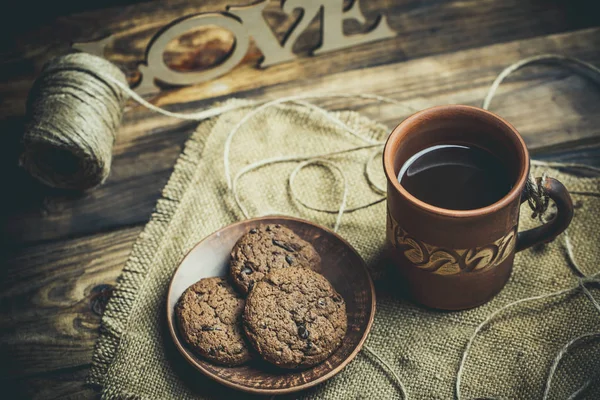 Kahverengi kil kahve fincanları ve ahşap bir masada sıcak renklerde lezzetli çikolatalı kurabiyeler.