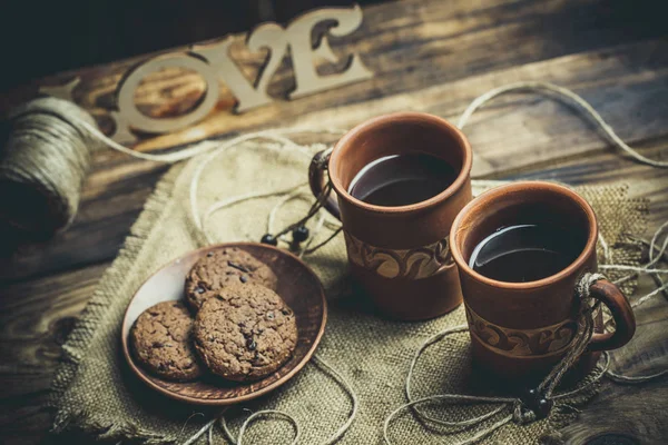 Kahverengi kil kahve fincanları ve ahşap bir masada sıcak renklerde lezzetli çikolatalı kurabiyeler.