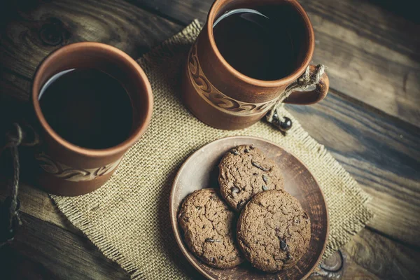 Kahverengi kil kahve fincanları ve ahşap bir masada sıcak renklerde lezzetli çikolatalı kurabiyeler.