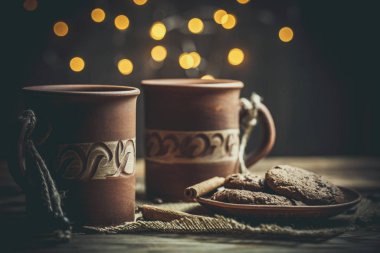 Kahverengi kil kahve fincanları ve ahşap bir masada sıcak renklerde lezzetli çikolatalı kurabiyeler.