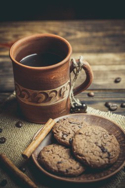 Kahverengi kil kahve fincanları ve ahşap bir masada sıcak renklerde lezzetli çikolatalı kurabiyeler.