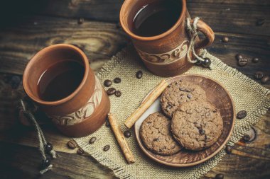 Kahverengi kil kahve fincanları ve ahşap bir masada sıcak renklerde lezzetli çikolatalı kurabiyeler.