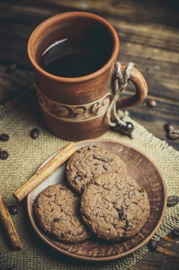 Kahverengi kil kahve fincanları ve ahşap bir masada sıcak renklerde lezzetli çikolatalı kurabiyeler.