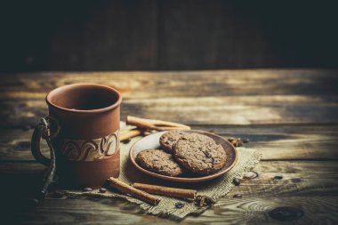 Kahverengi kil kahve fincanları ve ahşap bir masada sıcak renklerde lezzetli çikolatalı kurabiyeler.