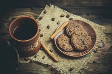 Kahverengi kil kahve fincanları ve ahşap bir masada sıcak renklerde lezzetli çikolatalı kurabiyeler.