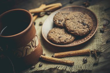 Kahverengi kil kahve fincanları ve ahşap bir masada sıcak renklerde lezzetli çikolatalı kurabiyeler.
