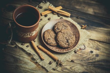 Kahverengi kil kahve fincanları ve ahşap bir masada sıcak renklerde lezzetli çikolatalı kurabiyeler.