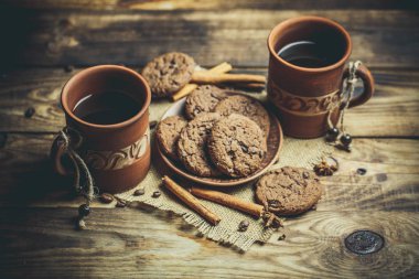 Kahverengi kil kahve fincanları ve ahşap bir masada sıcak renklerde lezzetli çikolatalı kurabiyeler.