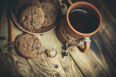 Kahverengi kil kahve fincanları ve ahşap bir masada sıcak renklerde lezzetli çikolatalı kurabiyeler.