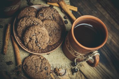Kahverengi kil kahve fincanları ve ahşap bir masada sıcak renklerde lezzetli çikolatalı kurabiyeler.