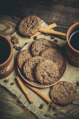 Kahverengi kil kahve fincanları ve ahşap bir masada sıcak renklerde lezzetli çikolatalı kurabiyeler.