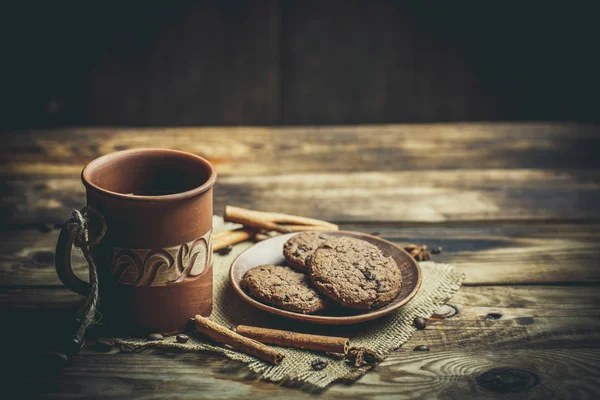 Kahverengi kil kahve fincanları ve ahşap bir masada sıcak renklerde lezzetli çikolatalı kurabiyeler.