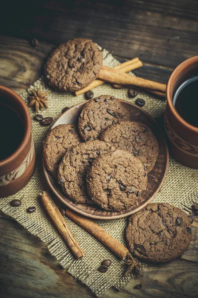 Kahverengi kil kahve fincanları ve ahşap bir masada sıcak renklerde lezzetli çikolatalı kurabiyeler.