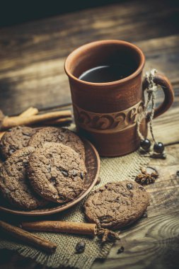 Kahverengi kil kahve fincanları ve ahşap bir masada sıcak renklerde lezzetli çikolatalı kurabiyeler.