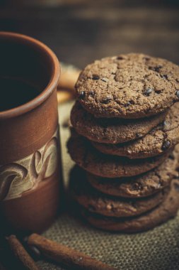 Kahverengi kil kahve fincanları ve ahşap bir masada sıcak renklerde lezzetli çikolatalı kurabiyeler.