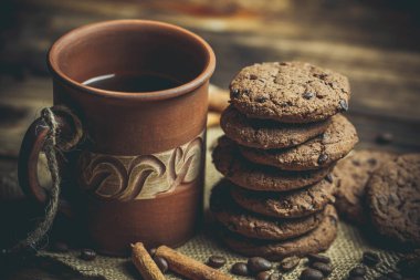 Kahverengi kil kahve fincanları ve ahşap bir masada sıcak renklerde lezzetli çikolatalı kurabiyeler.