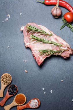 Kaşıklar, biberler, sarımsak, defne yaprağı, acı biber domatesleri ve siyah bir yüzey üzerinde büyük ve taze bir parça et.