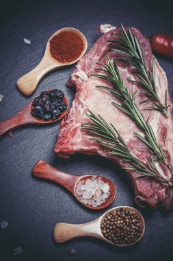 Kaşıklar, biberler, sarımsak, defne yaprağı, acı biber domatesleri ve siyah bir yüzey üzerinde büyük ve taze bir parça et.